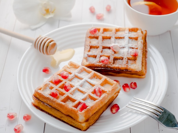 Heerlijke verrukkelijke Weense wafels met honing en granaatappelzaden op een witte plaat