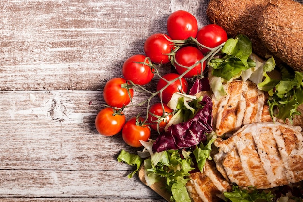 Heerlijke verse gegrilde kip op een houten bord naast gezond brood, tomaten en salade. gezonde levensstijl en eten