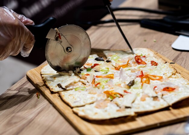 Foto heerlijke verse pizza, close-up van pizzasnijder op italiaanse pizza op houten lijst