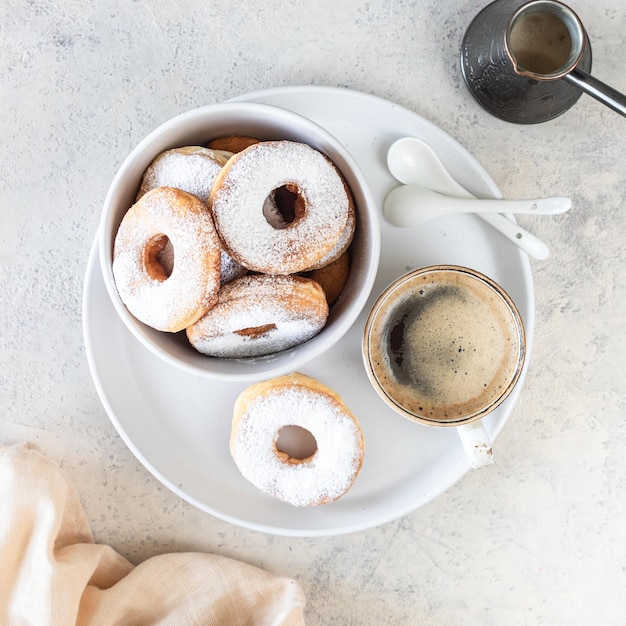 Heerlijke zelfgemaakte donuts met suiker en een kopje koffie op een vierkant met witte stenen achtergrond