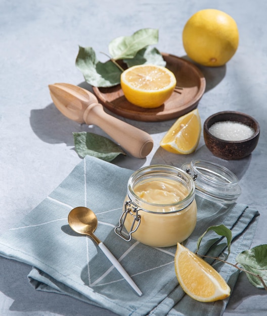 Heerlijke zelfgemaakte lemon curd in een glazen pot met schijfjes citroen op een blauwe achtergrond. Conceptontbijt met ochtendschaduw