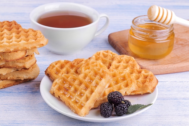 Heerlijke zoete Belgische wafels in de vorm van harten met honing en thee op een blauwe houten tafel. ontbijt.