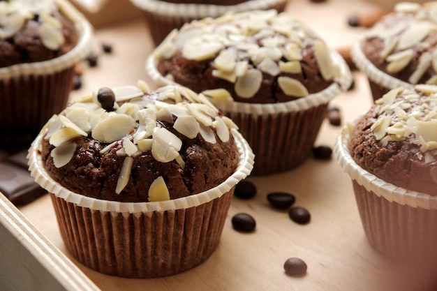 Heerlijke, zoete chocolademuffins, met amandelbloemblaadjes in een houten dienblad naast korrels van koffie op een blauwe houten tafel.