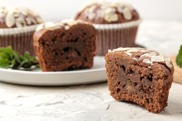 Heerlijke, zoete chocolademuffins, met amandelbloemblaadjes naast munt en amandelnoten op een lichte betonnen tafel. detailopname