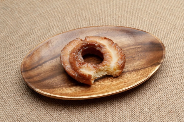 Heerlijke zoete donut gebeten op houten schotel geïsoleerd op jute achtergrond
