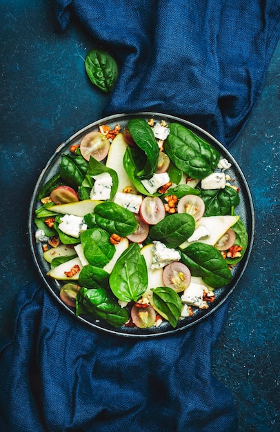 Heerlijke zomersalade met peer druiven roquefort kaas spinazie walnoten op blauwe tafel achtergrond bovenaanzicht negatieve ruimte