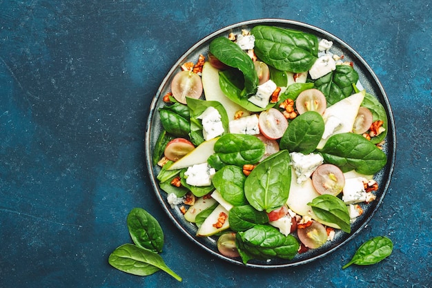 Heerlijke zomersalade met peer druiven roquefort kaas spinazie walnoten op blauwe tafel achtergrond bovenaanzicht negatieve ruimte