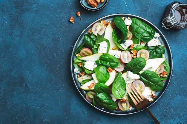 Heerlijke zomersalade met peer druiven roquefort kaas spinazie walnoten op blauwe tafel achtergrond bovenaanzicht negatieve ruimte