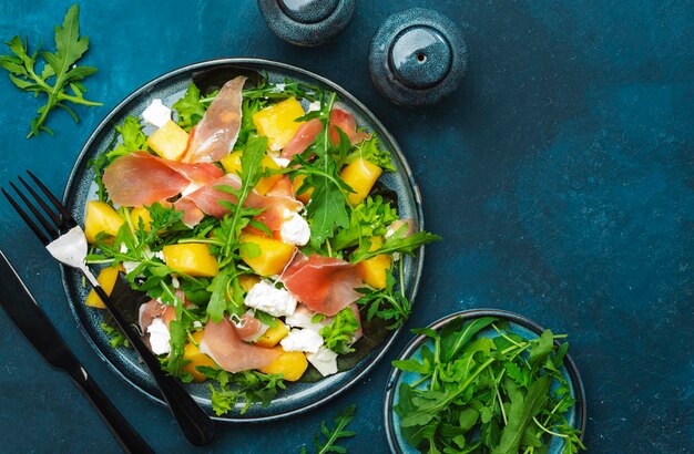 Heerlijke zomerse frisse salade met meloen meloen prosciutto zachte kaas en rucola op blauwe tafel achtergrond bovenaanzicht kopie ruimte