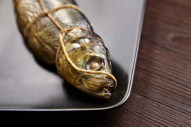 Heet gerookte vis, kipperharing. Twijn gebonden vis op zwarte plaat op bruin houten tafel, close-up