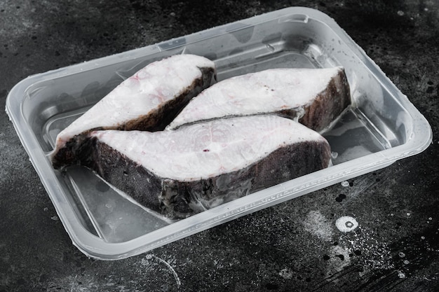 Heilbot vis bevroren steak pack set, op zwarte donkere stenen tafel achtergrond, met kopie ruimte voor tekst