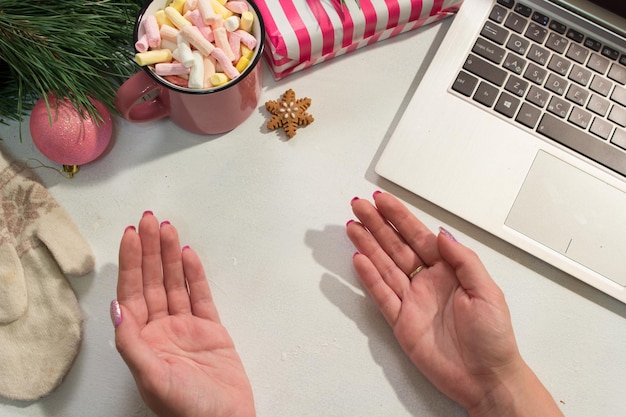 Heilwens in Kerstmis en Nieuwjaar vakantie Vrouw geopende handen in de buurt van feestelijk versierde grenen laptop en kopje marshmallows bovenaanzicht Groeten en presenteert concept