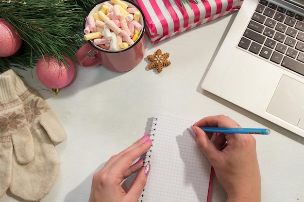 Heilwens in Kerstmis en Nieuwjaar vakantie vrouw schrijven brief in de buurt van feestelijk versierde grenen laptop en kopje marshmallows bovenaanzicht Groeten en cadeautjes in winter viering concept