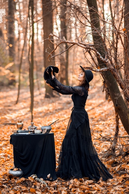 Heks in het herfstbos. Een vrouw met een zwarte kat bereidt zich voor op Halloween.