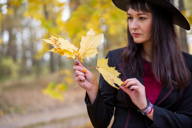 Heks in het herfstbos tovert gele gevallen esdoornbladeren op de achtergrond