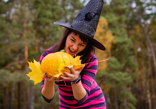 Heksenvrouw die pompoen met enge emoties vasthoudt in het herfstbos