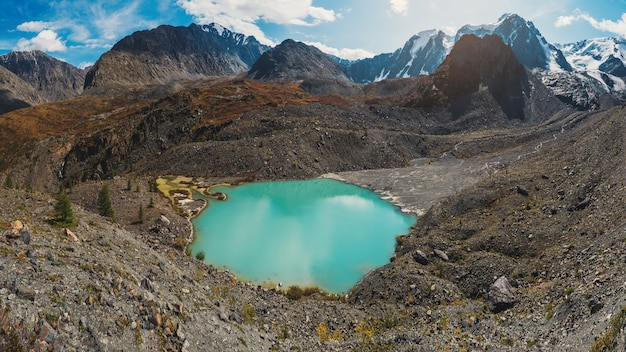 Helder alpenlandschap met bergmeer in hooglandvallei in zonlicht en grote berg onder blauwe bewolkte hemel. Schaduw van wolken op de herfstbergvallei. Panoramisch uitzicht.