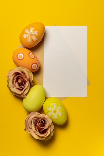 Foto helder en kleurrijke paaseieren en bloemen met een blanco groetekaartje op een lichtgele achtergrond