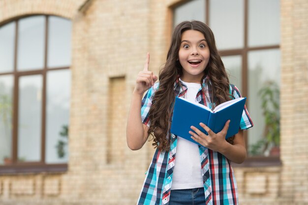 Helder idee Gelukkig kind met opgeheven vinger buitenshuis Klein kind houdt schoolboek vast Onderwijsactiviteiten Inspiratie en creativiteit Creatief en innovatief idee Leren denken Heb een idee