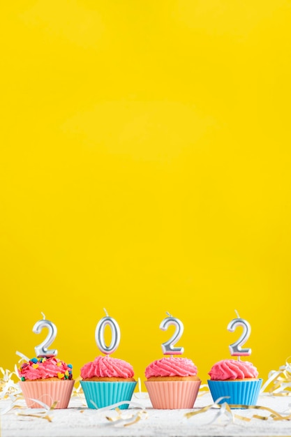 Helder kerstthema met kaarsen in de vorm van nummers 2022 op cupcakes op gele achtergrond. Ruimte kopiëren.