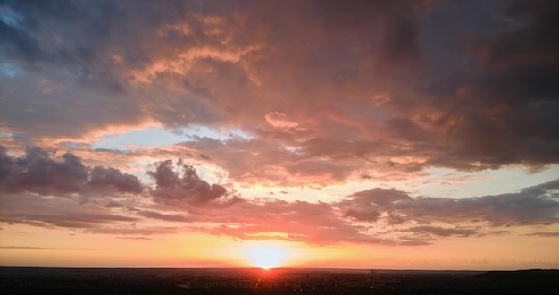 Helder kleurrijke zonsondergang hemel met ondergaande zon en levendige wolken over donker landschap