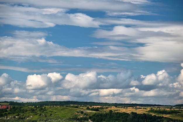 Foto helder landschap van witte gezwollen cumuluswolken op blauwe heldere hemel boven landelijk gebied.