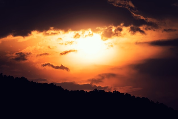 Helder oranje avond zonsondergang. Silhouetbomen temidden van ondergaande zon. donkere lucht met bewegende wolken. Dageraad over de bergen op een eiland in tropisch Azië.