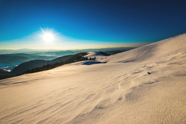 Helder pittoresk zonnig panorama van de skipistes op de achtergrond van de vallei en de heuvels en het dichte bos op een ijzige winterdag. Skigebied concept. Advertentie ruimte