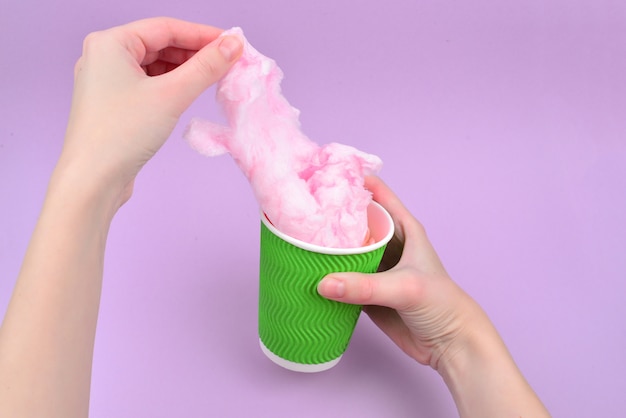 Helder roze suikergoedkatoen in plastickkop in vrouwenhand