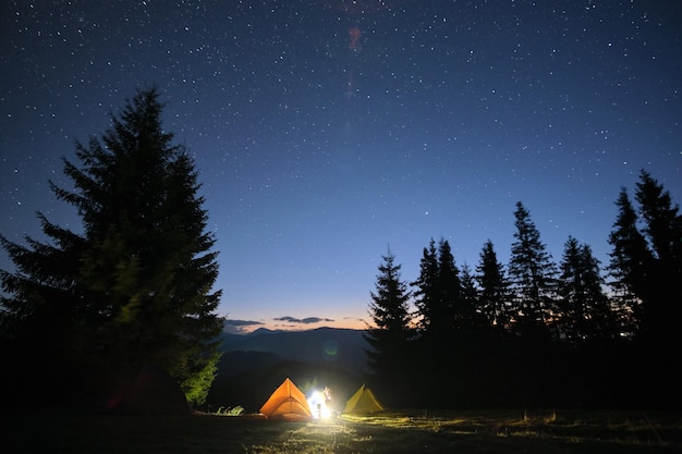 Helder verlichte toeristententen gloeien op de camping in donkere bergen onder de nachtelijke hemel met fonkelende sterren Actief levensstijlconcept