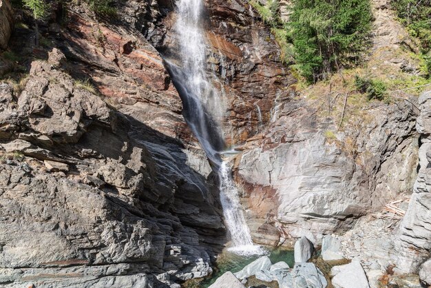 Helder zicht op de stromende Lillaz-waterval met de resulterende vijver eronder en granieten karstrotsen in Aosta