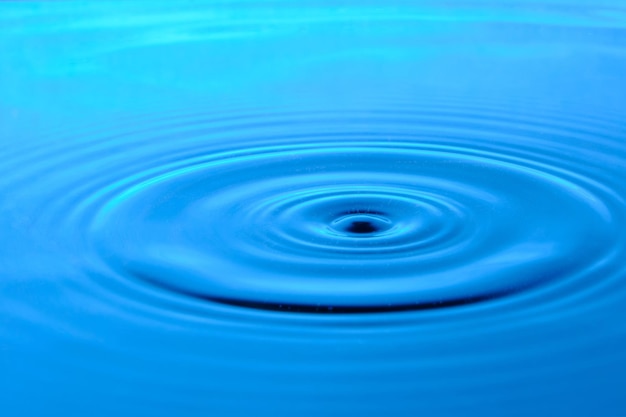 Helderblauwe achtergrond met divergerende cirkels van een druppel op het oppervlaktewater.