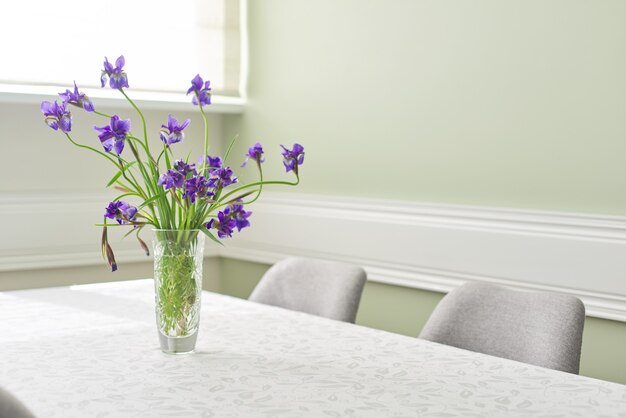 Heldere eetkamer interieur, tafel en stoelen in de buurt van raam, boeket van paarse irissen in vaas, wit tafelkleed ruimte, kopie ruimte