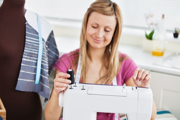 Heldere jonge vrouw die haar naaimachine met behulp van