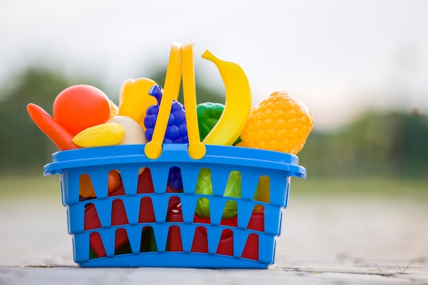 Heldere plastic kleurrijke mand met stuk speelgoed fruit en groenten in openlucht op zonnige de zomerdag.