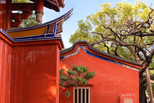 Heldere rode muur van Chinese tempel met traditionele patronen, een oude boom erachter.