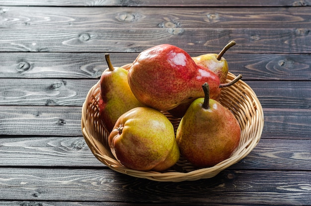 Heldere rood-gele peren in een mand op een donkere houten rustieke achtergrond. Herfstoogst van fruit.