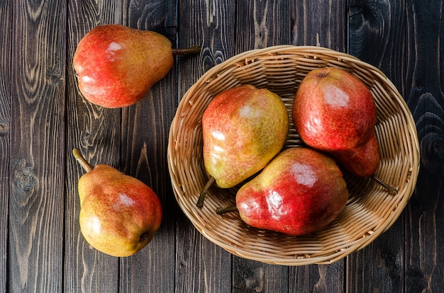 Heldere rood-gele peren in een mand op een donkere houten rustieke achtergrond. Herfstoogst van fruit.