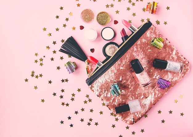 Heldere samenstelling van modeaccessoires. Glitter pailletten make-up tas met lipsticks, nagellakken en andere voorwerpen. Bezwaar op zachte pastelachtergrond met decoratief klatergoud. Plat lag, bovenaanzicht.