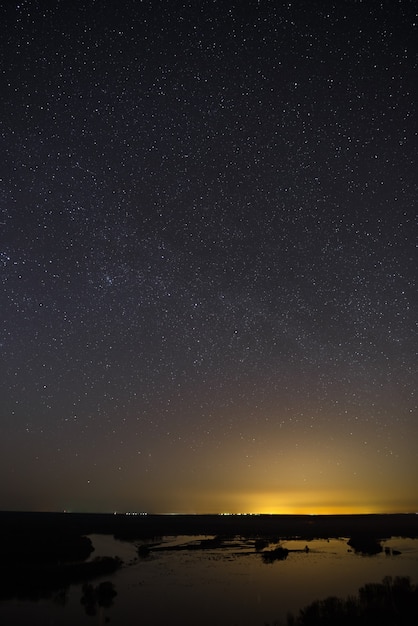 Heldere sterren van de nachtelijke hemel tegen de achtergrond van het gladde oppervlak van het meer.