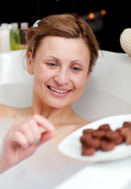 Heldere vrouw die chocolade eet terwijl het hebben van een bad