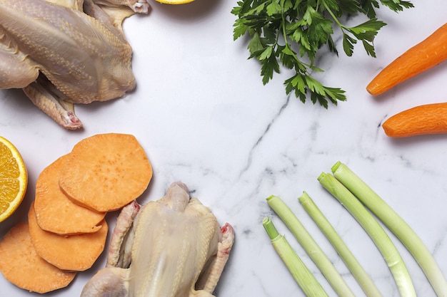 Hele coquelet-kippen met rauwe groenten, klaar om te koken. Wortelen, prei; zoete aardappel; peterselie van bovenaf. Plat leggen