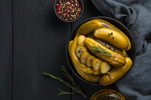 Hele en gesneden ingelegde komkommers met peper en rozemarijn in een kom op een houten achtergrond. Bovenaanzicht, kopieer ruimte.