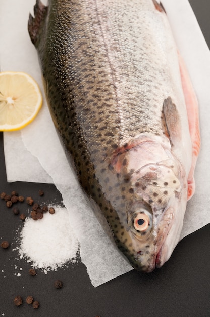 Hele forel, citroen, zout en peper op een zwarte achtergrond