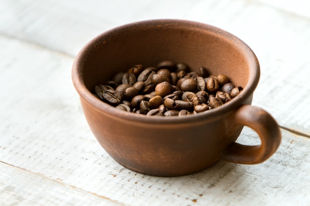 Hele koffiebonen in de bruine kop die op een houten vloer staat