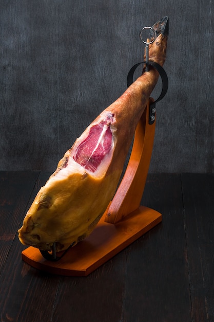Hele mediterrane traditionele jamon op een houten standaard met een mes leun op een tafel donker beeld