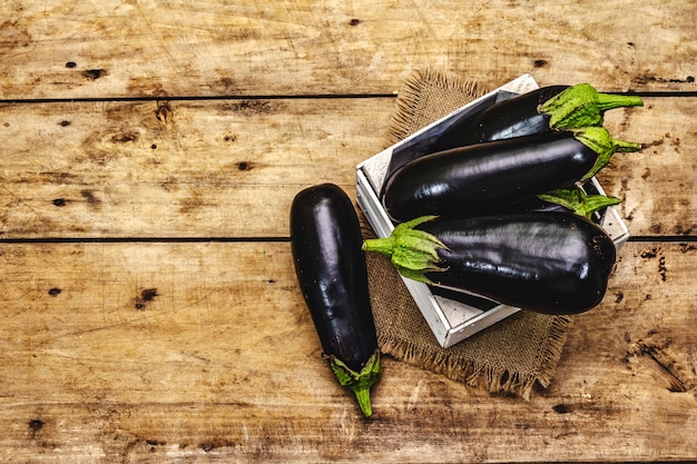 Hele ongepelde rauwe aubergines in een houten kist. Nieuwe oogst, op zak, houten planken achtergrond, bovenaanzicht