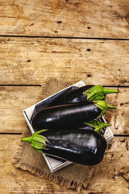 Hele ongepelde rauwe aubergines in een houten kist. Nieuwe oogst, op zak, houten planken achtergrond, bovenaanzicht