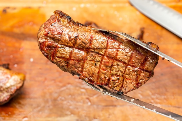 hele picanha-biefstuk op snijplank en metalen tang