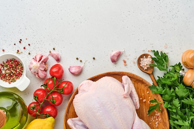 Hele rauwe kip met ingrediënten voor het maken van rozenpeper, citroen, tijm, knoflook, cherrytomaat, zuring en zout in de keuken op lichtgrijze leisteen, steen of betonnen ondergrond. Bovenaanzicht